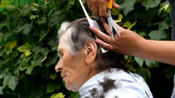 istock Cutting senior woman hair with scissors at home while quarantine 1296221234