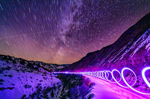 Light Painting Mountain Astrophotography - Night view along desolate road with snow and mountain views. Light painting patterns and long exposure with star trails.