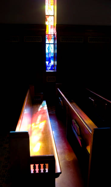 istock Light coming through stained glass window lighting pews with colorful light 1296225584
