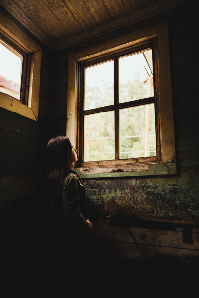 istock Young woman looking through the window in an old room 1296228884