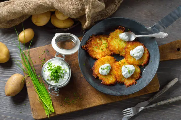 Crunchy potato pancakes with sour cream and fresh chives served in an iron frying pan