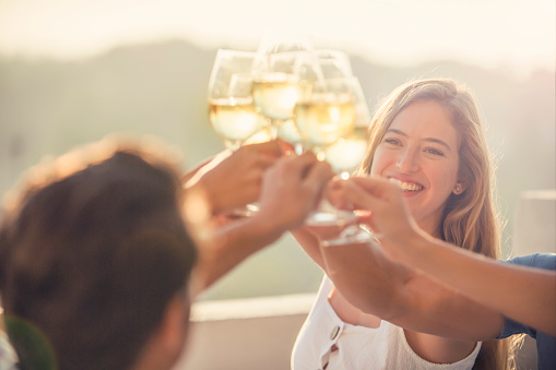 Group of friends drinking wine and making a celebration toast outdoors. A woman can be seen happy and smiling. Back lit at sunrise or sunset.  Focus on background