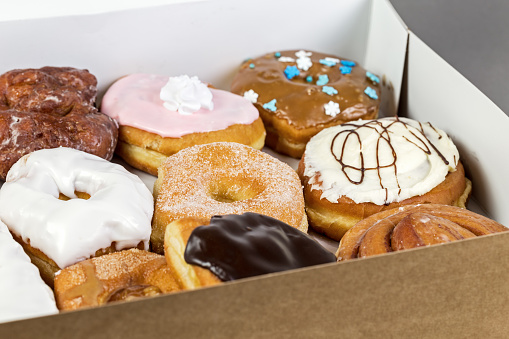 A take out food box full of assorted donuts with icing and sugar.