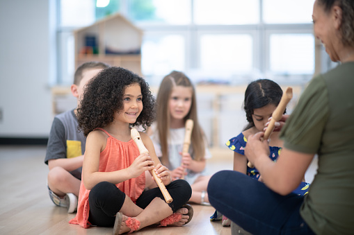 An adorable preschool girl of mixed race ethnicity smiles while holding a flute in her preschool classroom.