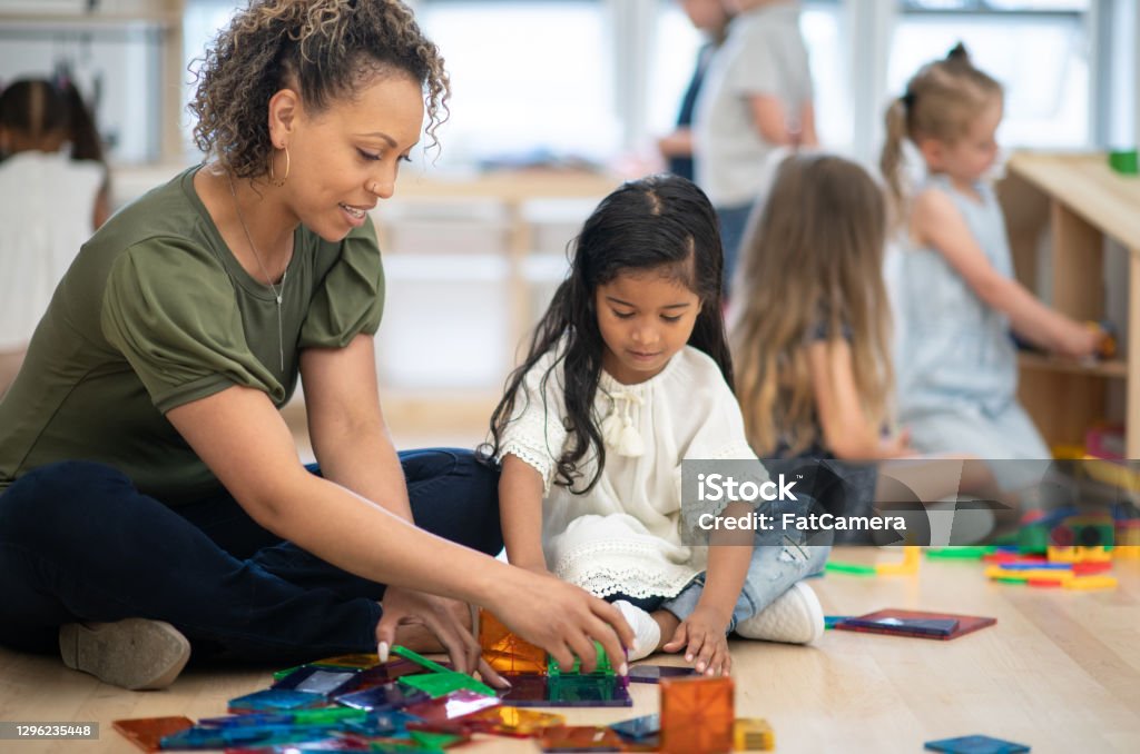 Thank you for your help, teacher! A female preschool teacher of African ethnicity helps one of her students build a tower using magnetic tiles. Child Care Stock Photo