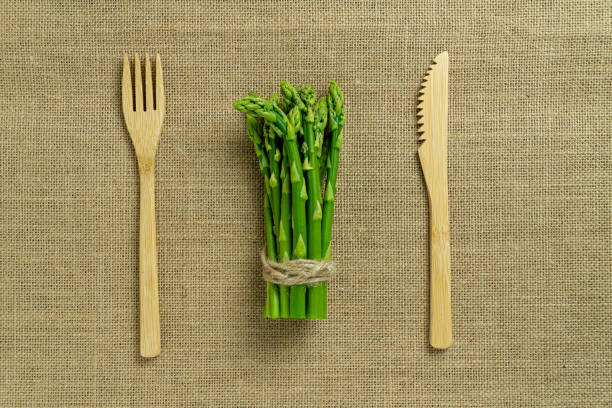 Bunch of fresh green asparagus with disposable wooden fork and knife on a rough canvas background. Flat lay top view. Cooking concept for blog or recipe book. stock photo
