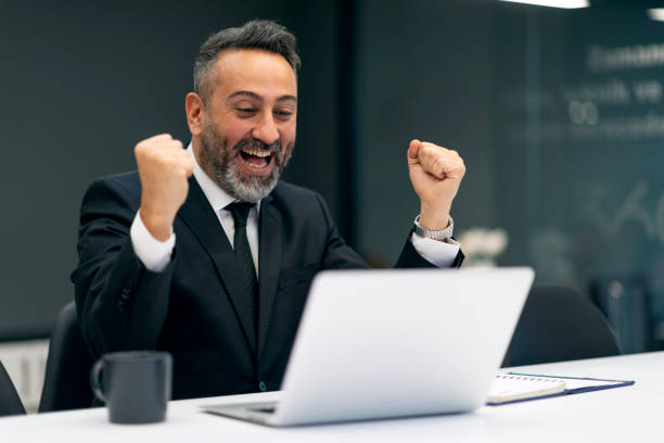 ラップトップで良いニュースを読んで有頂天のビジネスマン - ガッツポーズ ストックフォトと画像