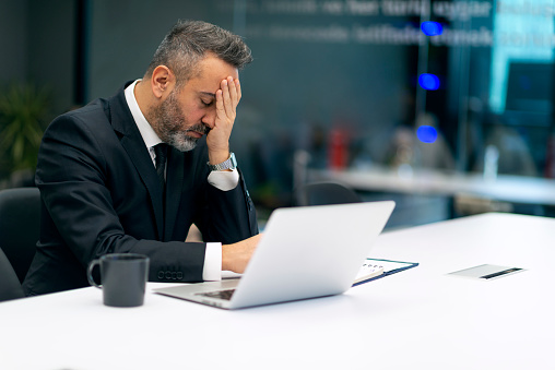 Shocked upset worried businessman reading bad news on laptop in the office.