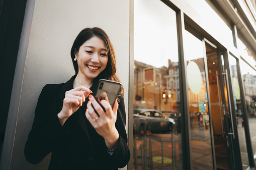 Asian business woman using her smartphone on the street for communicating with his business partners.\nSmartphone has become an essential tool for everyday life.