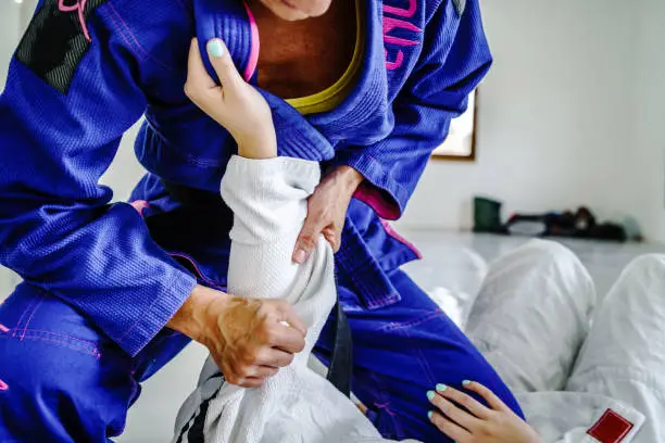 Grips from the guard in brazilian jiu jitsu bjj or judo training sparring two female women athletes fighters drilling techniques for the competition advanced guard holding kimono gi for self-defense