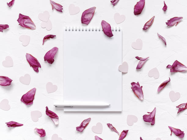 Open blank notebook, pen, peony petals, heart-shaped confetti are on a textured background. Floral layout for Valentine's day. Flat lay. Top view. Copy space. stock photo