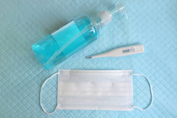 istock Closeup mercury, white mask and blue alcohol gel bottle on blue plastic background, top view, concept supplies for protection outbreak corona virus (covid19) 1296263718