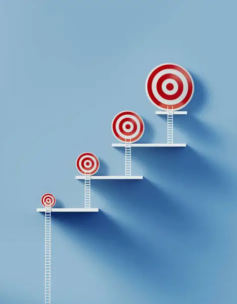 White ladders leaning over different sized bull's eye targets on blue wall. Vertical composition with copy space. Aspirations, determination, goals and strategy concept.