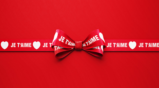 I Love You ( Je T'aime in French ) written red ribbon over red background. Horizontal composition with copy space. Copy space available. Valentine's Day concept.