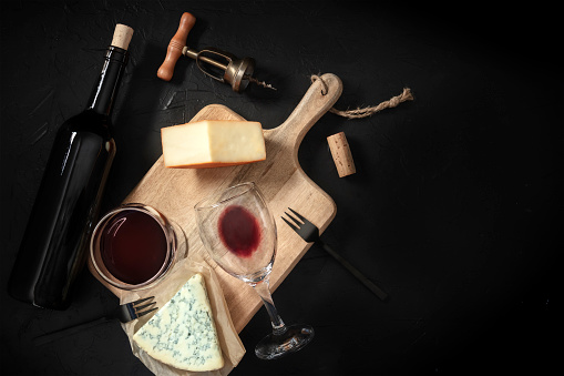 Wine and cheese tasting, overhead shot on a black background, with a vintage corkscrew and a bottle, with a place for text