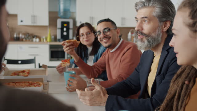 Diverse group of people coworkers talking and laughing eating pizza in workplace