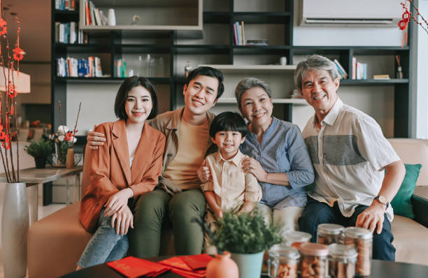 familia china de año nuevo de varias generaciones sentada en la sala de estar del sofá mirando a la cámara sonriendo feliz - cultura asiática fotos fotografías e imágenes de stock