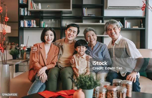 Chinese New Year Multi Generation Family Sitting On Sofa Living Room Looking At Camera Smiling Happy Stock Photo - Download Image Now