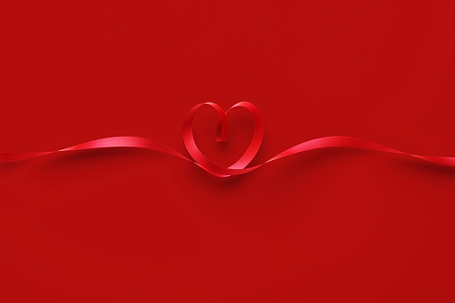 Red ribbon forming heart shape over red background. Horizontal composition with copy space. Valentine's day  concept. Copy space available