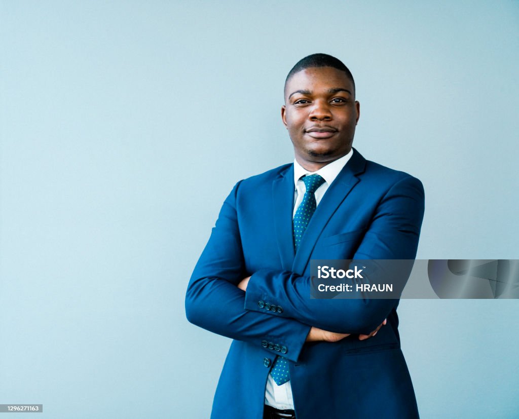 Confident businessman with arms crossed Portrait of confident businessman with arms crossed. Male entrepreneur is wearing blue suit. He is standing against gray background. Men Stock Photo