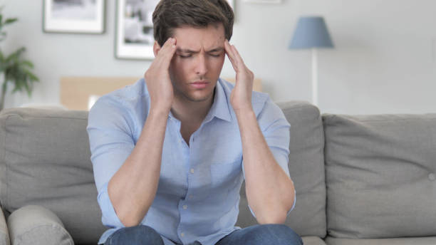 istock Handsome Young Man with Headache Sitting Tense on Couch 1296271911
