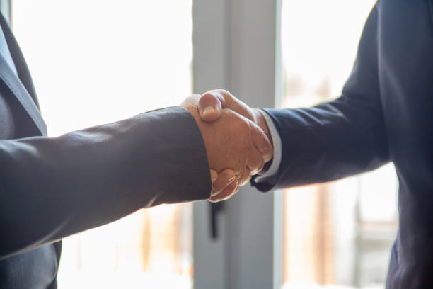 istock Businessmen in formal suits shaking hands in office 1296272904