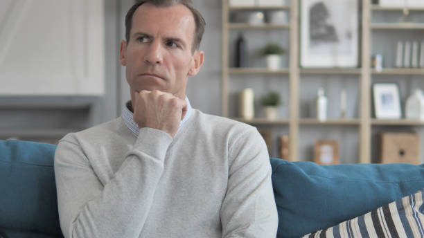 istock Pensive Creative Man Sitting on Couch and Lost in Thoughts 1296273205