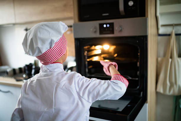 istock Boy in chef's whites and baker cap playing by the oven 1296273955