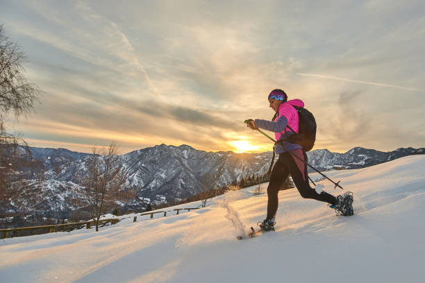 молодая спортивная женщина спускается по снегу со снегоступами в пейзаже заката - winter snowshoeing running snowshoe стоковые фото и изображения