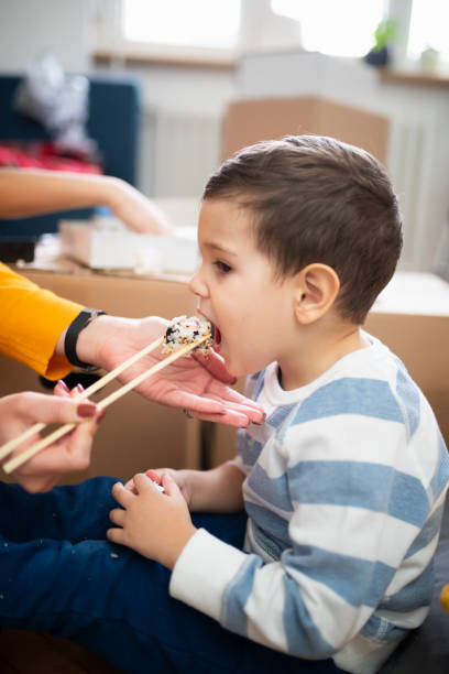 enfant en bas âge avec le sushi ouvert de bouche nourri sur des baguettes par sa mère - family mouth open vertical mother photos et images de collection