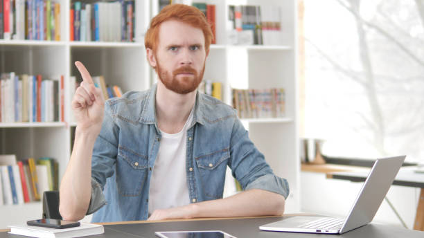 istock Young Casual Redhead Man Waving Finger to Reject at Work 1296274830