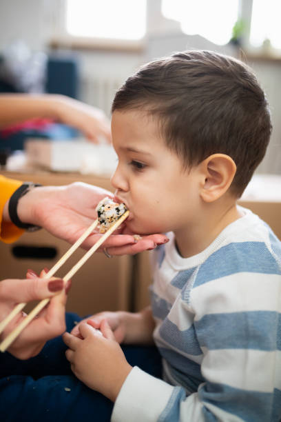 istock Toddler biting sushi roll in chopsticks held by his mother's hand 1296274843