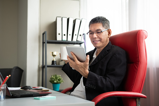 A successful confidence Asian businessman checking online stock market information using digital tablet in the office. 5G & Wireless Technology, Finance & Economy, Business ownership & Entrepreneurship, Financial Freedom Concepts.