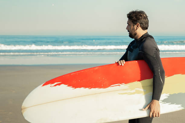 istock Concentrated man carrying surfboard and walking along coastline 1296275368