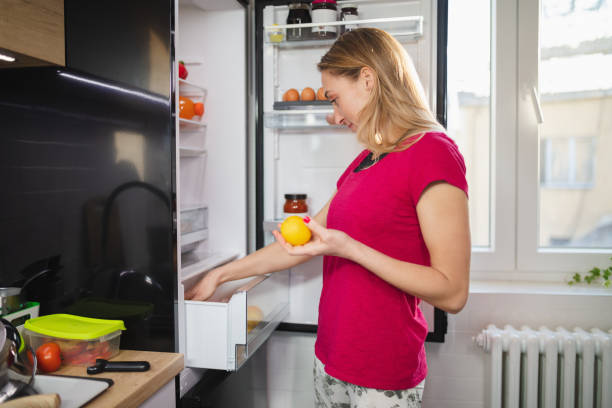 istock Woman by the open fridge holding lemon and taking ingredients from drawer 1296276024