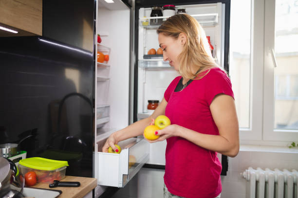 istock Woman by the open fridge holding lemon and taking apple from drawer 1296276044