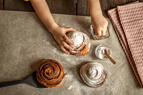 istock Children's hands in the frame sprinkles a fresh baked bun with cinnamon with pastry sprinkles 1296276252