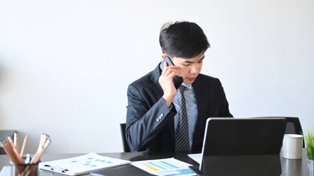 istock Businessman in formal clothes working on tablet compute and talking on phone discussing business matters in office. 1296276386