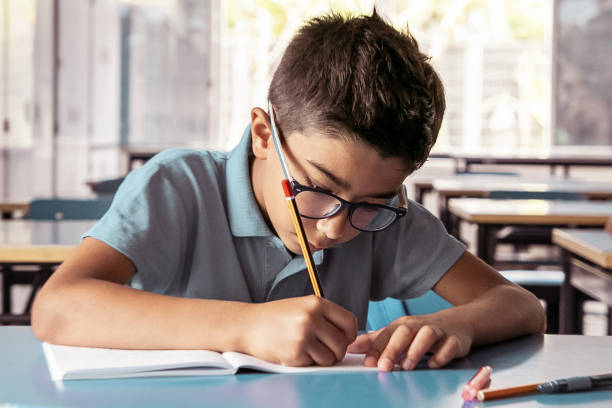 istock Focused young boy in glasses sitting at desk and writing 1296278158