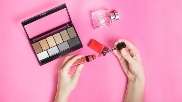 istock makeup concept. female hands open liquid lipstick on a pink background, close-up. 1296281415
