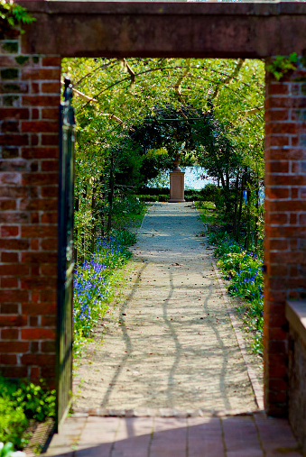 New Bern, North Carolina / USA - April 1, 2017: One open wrought iron gate leads to a trellis covers a pathway in the formal gardens on the grounds of historic Tryon Palace.