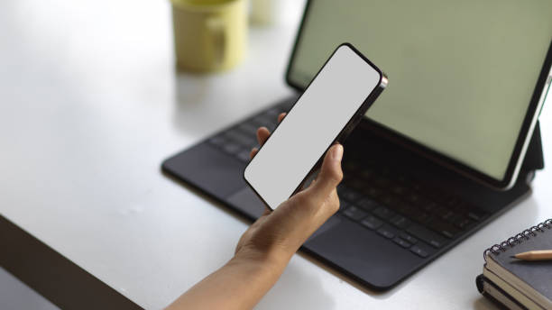 istock Female hand holding smartphone while working with tablet on the table 1296287153