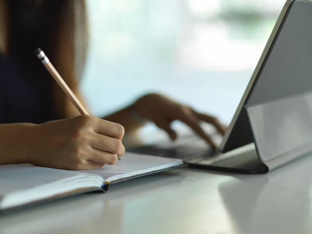 istock Female hand writing on notebook while working with laptop on the table 1296288508