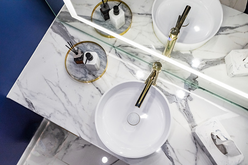 A modern bathroom with gold coloured faucet and round sink with marble tiles.