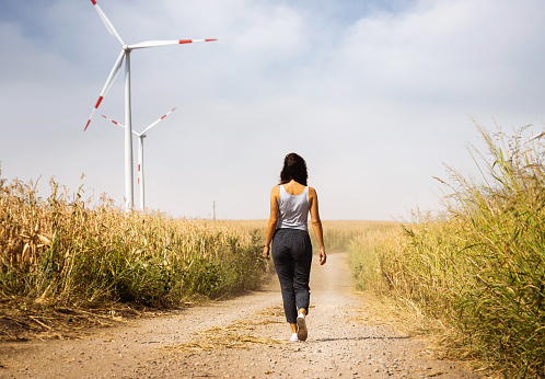 Woman walking on country road through fields with electric windmills in background