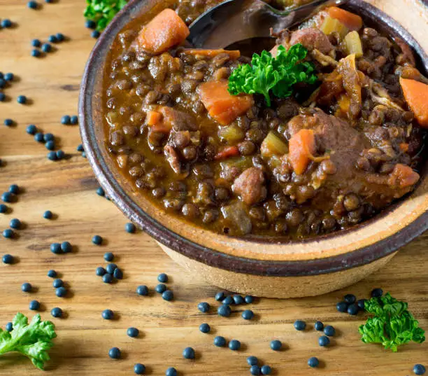 fresh cooked spicy beluga lentil stew with root vegetables and chicken meat. low fat and healthy meal on wooden table background