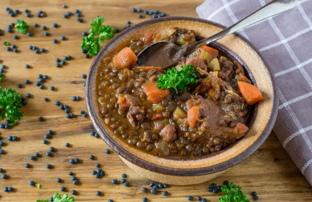 a bowl of fresh cooked healthy lentil soup with beluga lentils, root vegetables and low fat chicken meat served in a brown bowl on wooden table from above