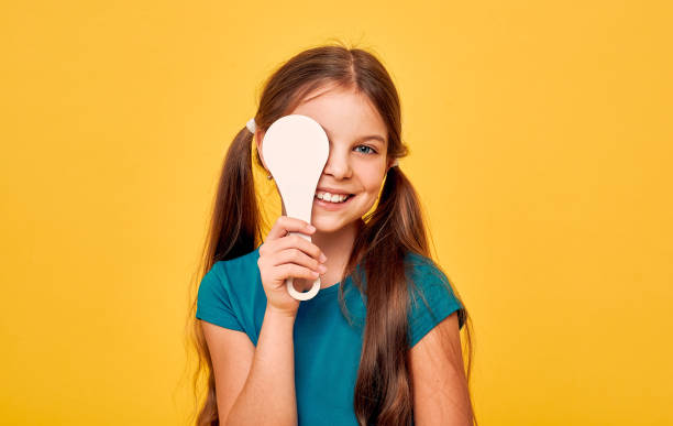 istock Smiling girl having eye exam with one eye covering using a special ophthalmic tool, on a yellow background. Eye test for child 1296294448