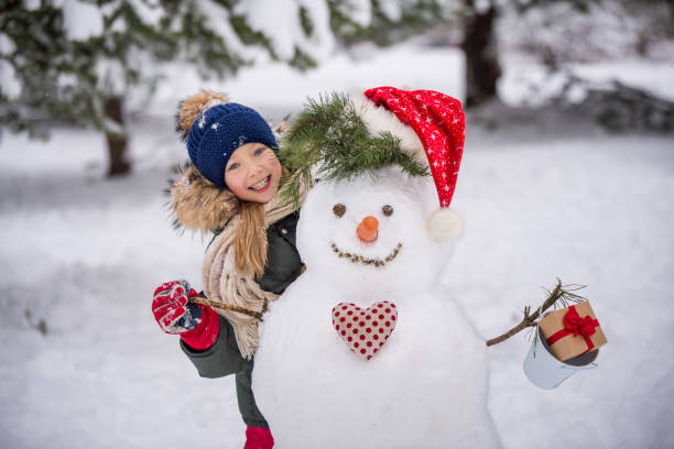 Happy girl child plaing with a snowman on a snowy winter walk stock photo