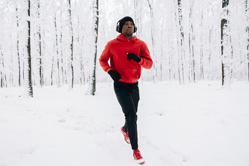 Young african american man running on winter day in forest